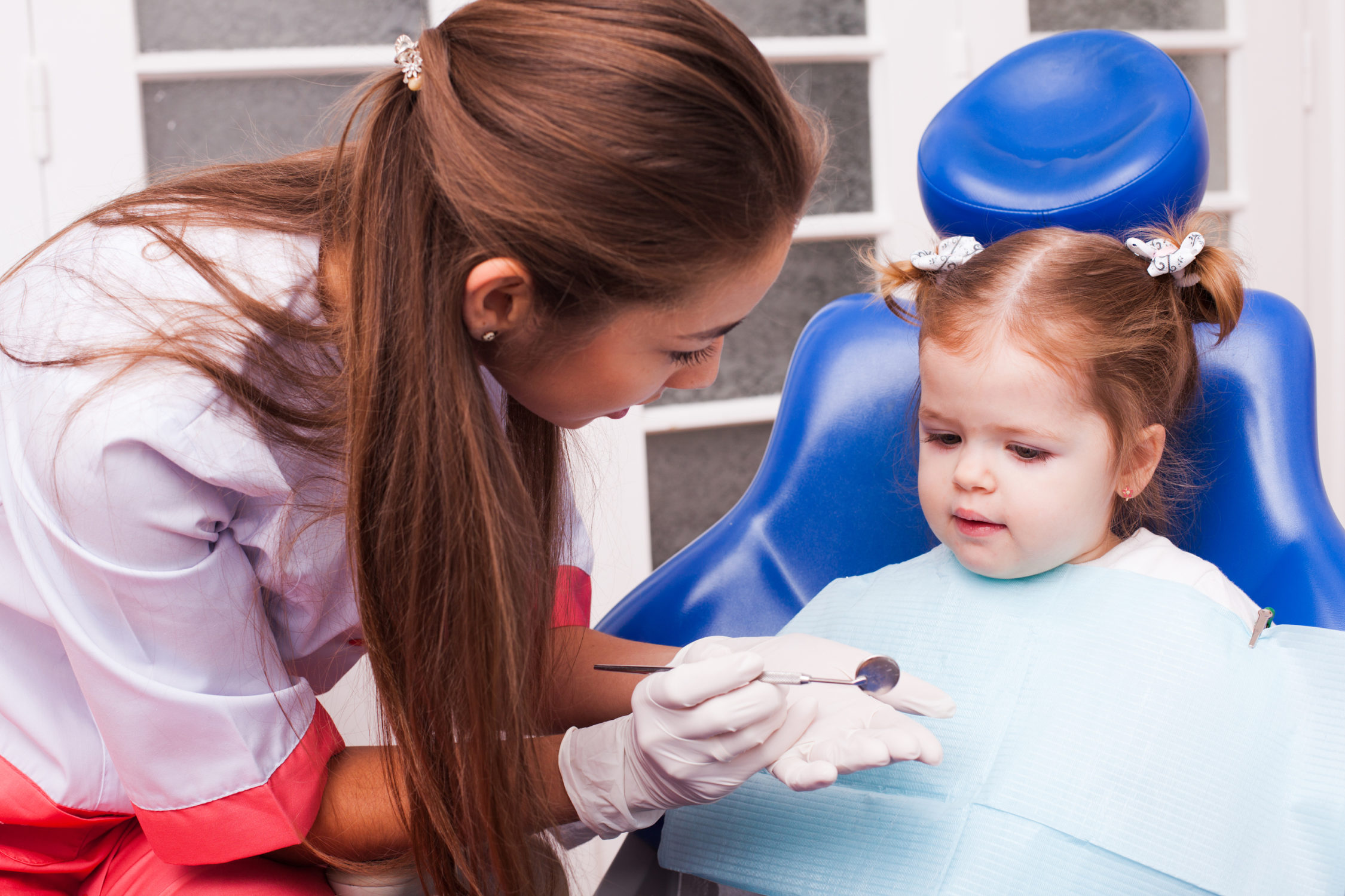 Two years old girl is on the first visit in the dental office. Young attractive dentist woman